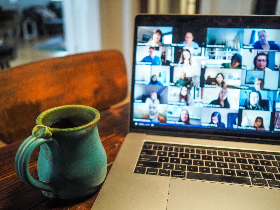 A green cup placed next to a laptop with a zoom meeting on its screen.
