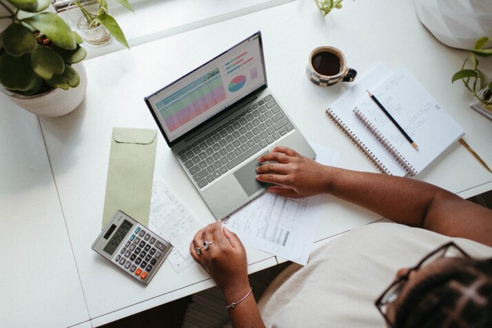 A busy work table with a laptop, calculator, and other documents.