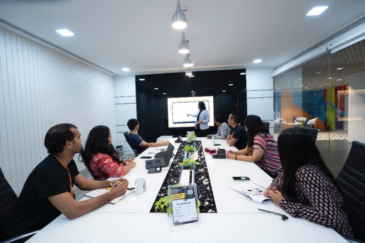 A group of employees seated on a long table while listening to a presentation.