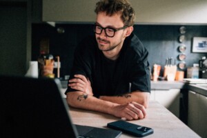 A man wearing a black shirt staring at his laptop in the kitchen.