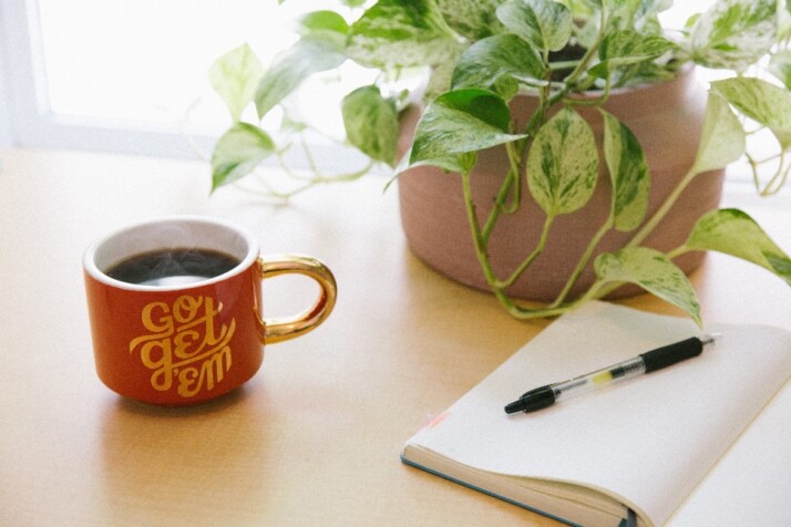 An open notebook next to a cup of coffee and a potted plant