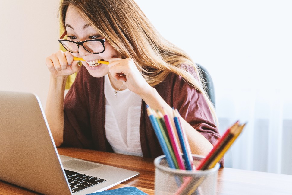 Concentrated woman biting pencil in front of laptop screen.