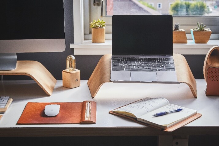 A busy work station with tons of work stuff including a laptop and a notebook.