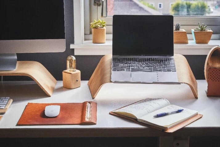 A busy work station with tons of work stuff including a laptop and a notebook.