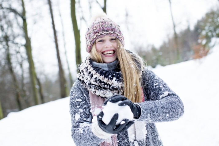Lady wearing sweater and cap holding snow in both hands