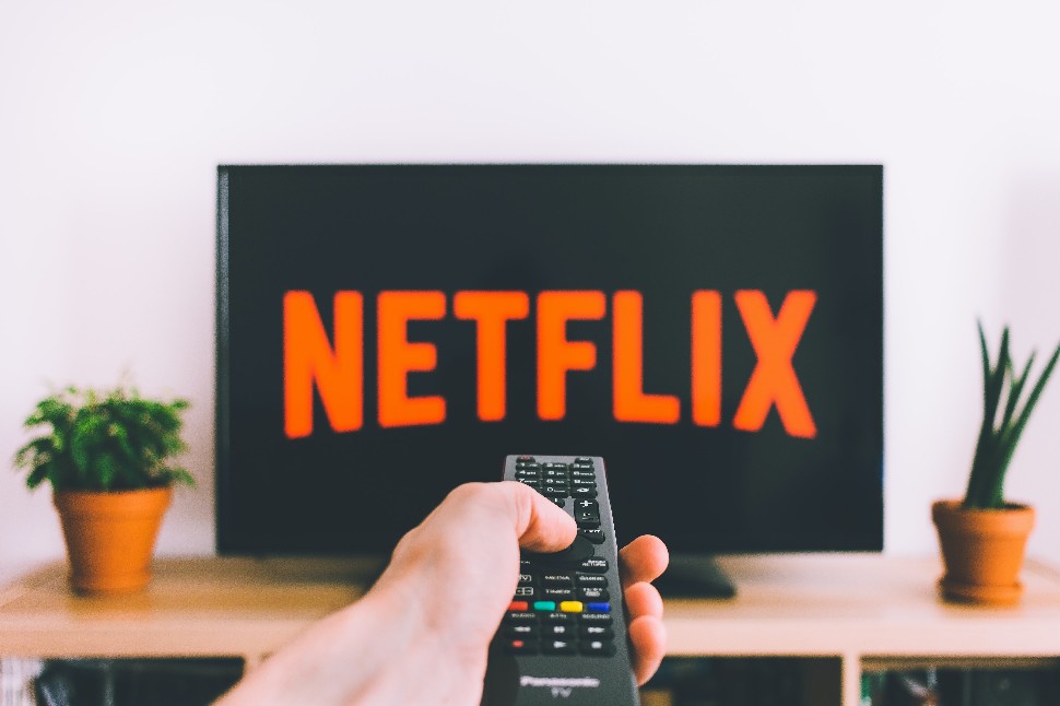Man holding TV remote control while Netflix plays on screen.
